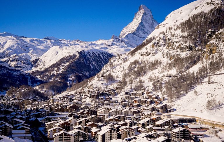 Snötäckt bergslandskap med Matterhorn i bakgrunden och en byn Zermatt nedanför.