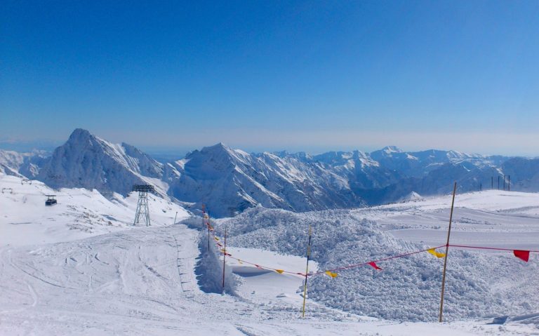 Vinterlandskap med snöklädda alpfjäll och klarblå himmel. Spår och hiss pyloner syns.