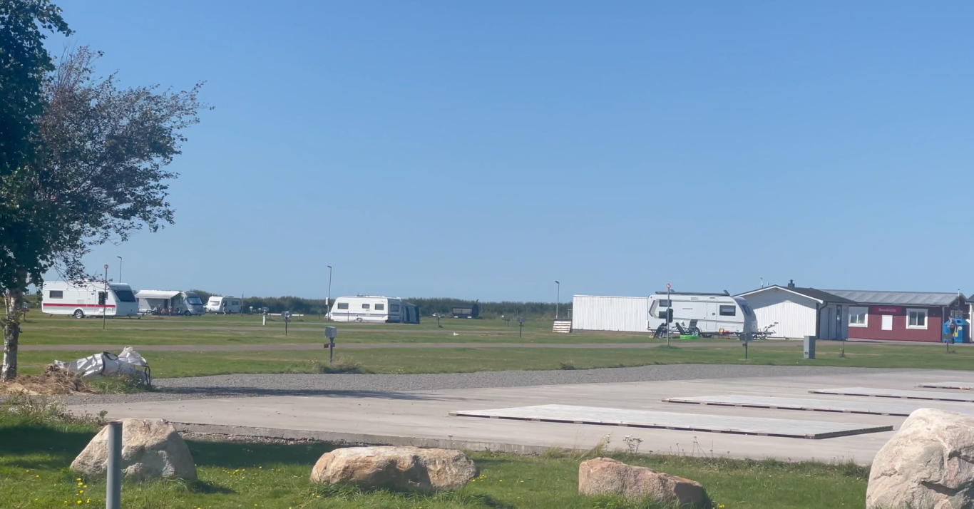 Björkängs Camping Landskap med campingvagnar och grönskande ängar under klar blå himmel.