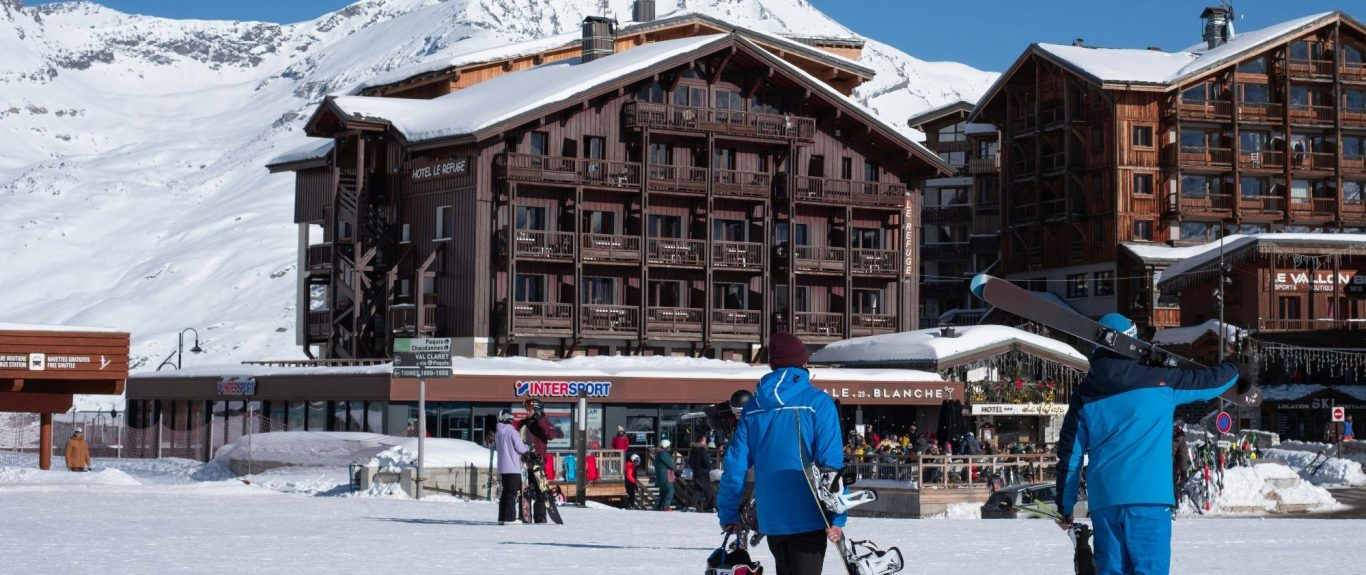 Skidåkare framför fjällstuga i snöig alpskulptur. Klara himmel och snötäckta berg.
