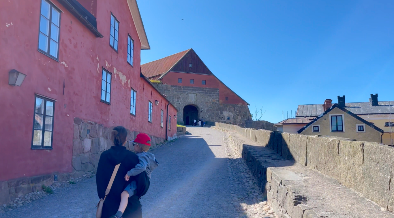 Varbergs Fästning Gata med röd husfasad som leder upp till ett slott under klarblå himmel.