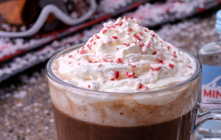 Kopp med kaffedryck toppad med grädde och röd-vita strössel. Snöig bakgrund.