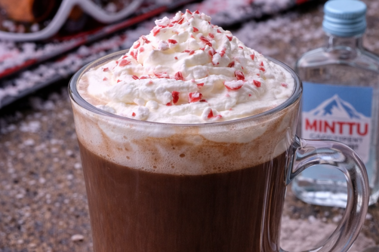Kopp med varm choklad, grädde och strössel, med en flaska vatten bredvid.
