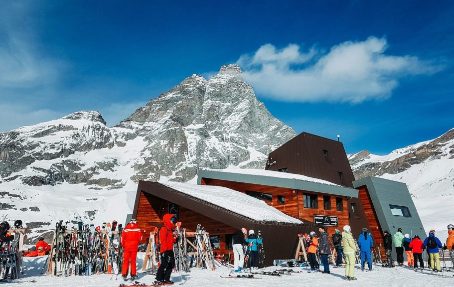 Backstage av en skidanläggning med alpfjäll i bakgrunden och människor som åker skidor.