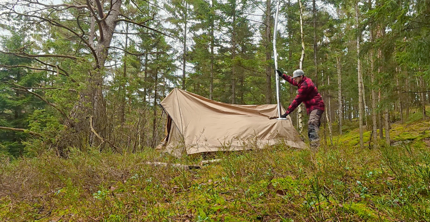 Monterar skorstenen Person reser ett tält i en grönskande skog med träd i bakgrunden.