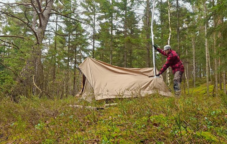 En person reser ett tält i en skogsmiljö.