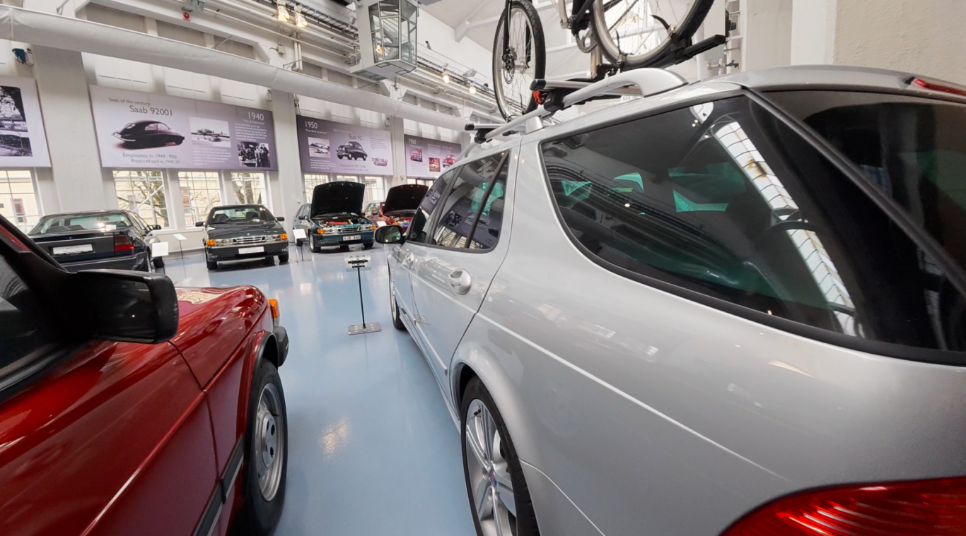 Saab 9-5 Bilutställning med en silverfärgad bil med cykelställ och flera andra bilar i bakgrunden.
