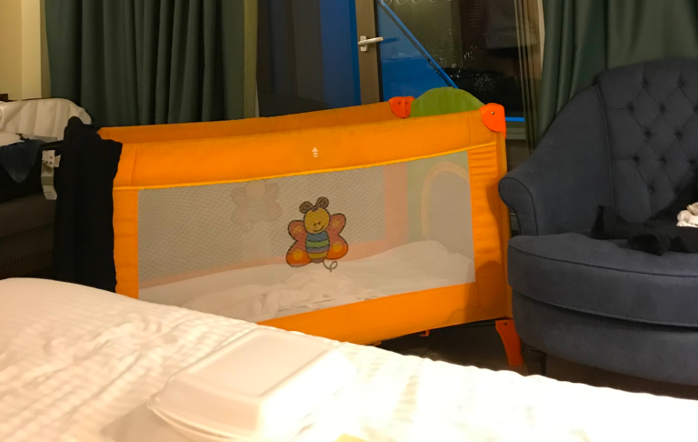 En orange spjälsäng med nätväggar står i ett rum bredvid en blå soffa.