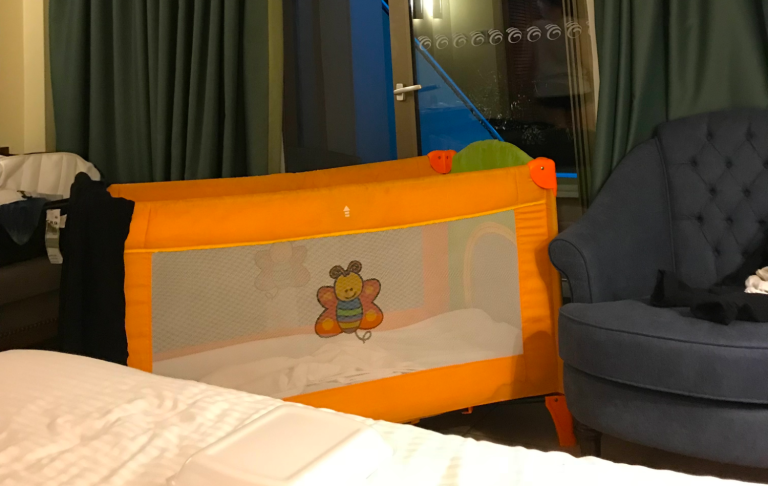 Barnsäng av orange färg med nätpanel och leksaksmotiv, placerad i ett rum.