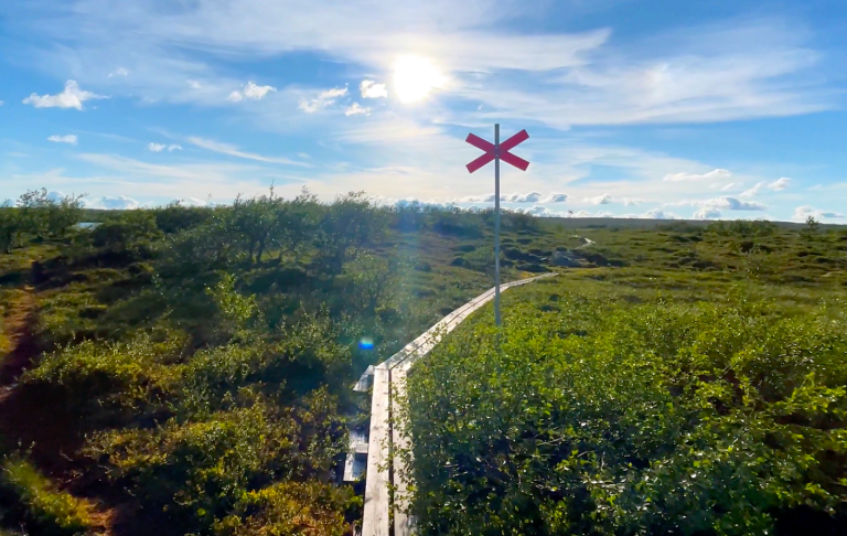 Röd korssignal på en grön kulle under en blå himmel med vita moln.