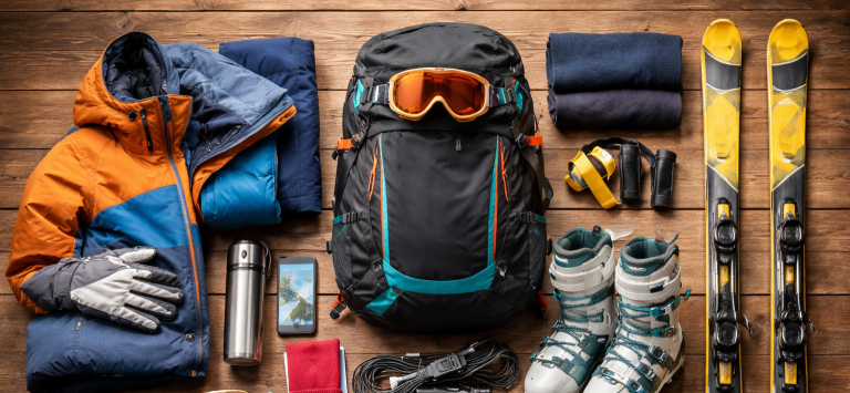 Utrustning för skidåkning med kläder, skidor, hjälm och vattenflaska på en träyta.