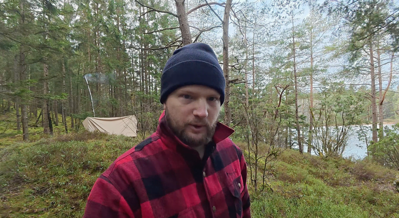 Hämtar vatten Man i röd och svart rutig skjorta med mössa, stående i en skogsmiljö.