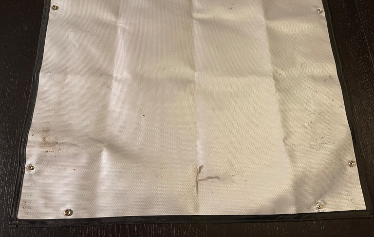 Sammetsaliknande vit pappersduk med några fläckar och hål i hörnen.