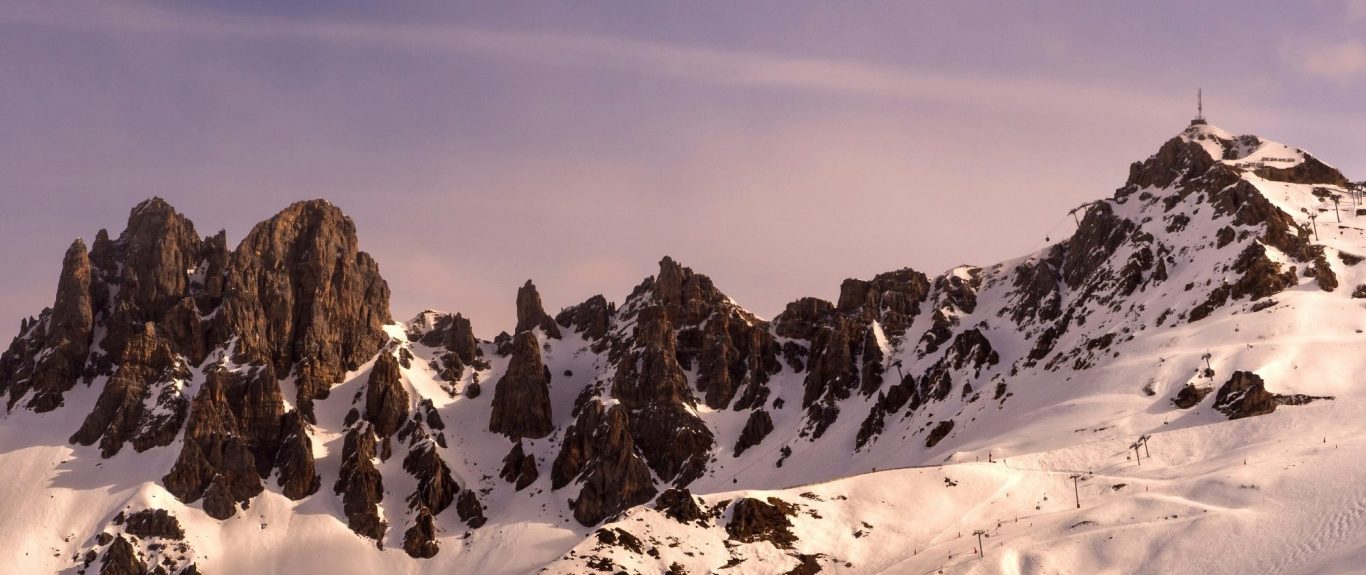Snöbeklädda alpbergtoppar med skarpa klippor och en mjuk ljusrosa himmel.