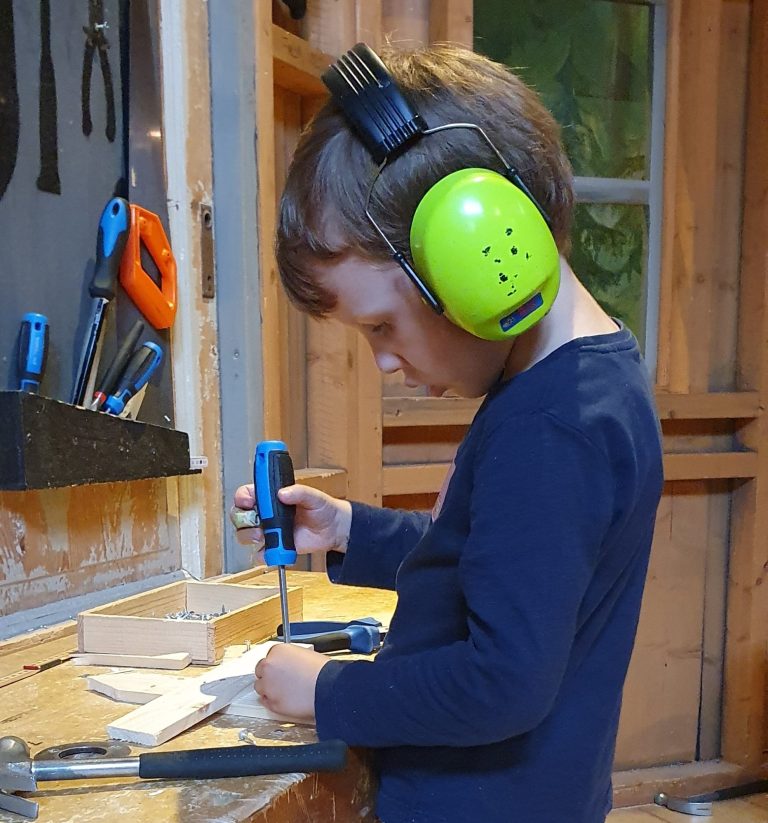 Ett barn med hörselskydd som skruvar i en träverkstad.