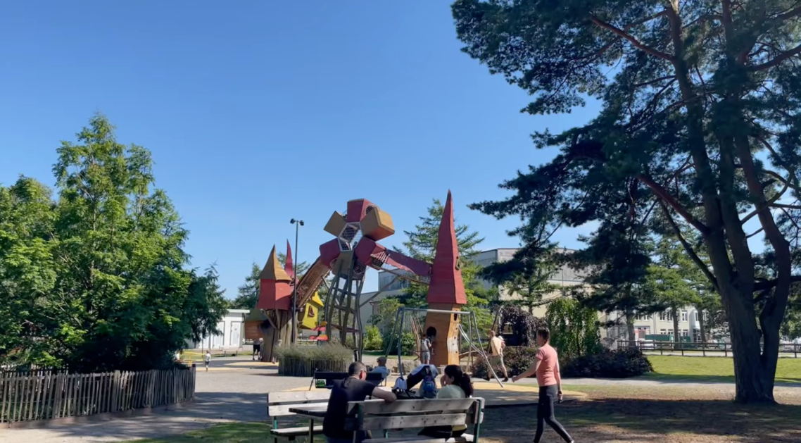 Vallarnas Friluftsområde Lekplatsen Barn leker vid en stor lekställning i en park under blå himmel.