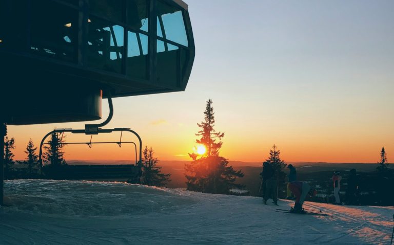 Solnedgång bakom snötäckta träd vid en skidanläggning med stollift.