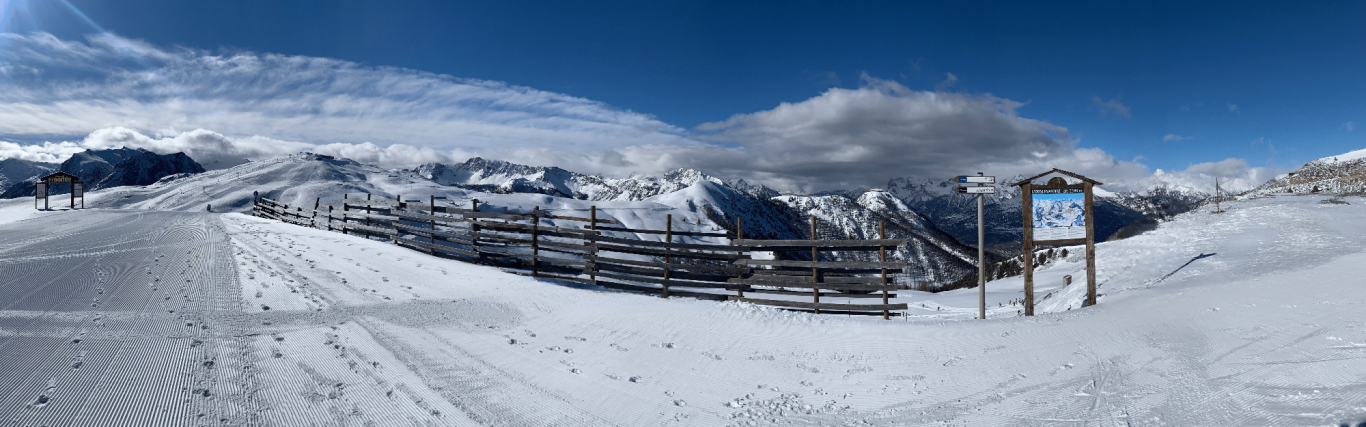 Vinterlandskap med snötäckta alpberg och en skylt vid skidbacke i italienska alperna.