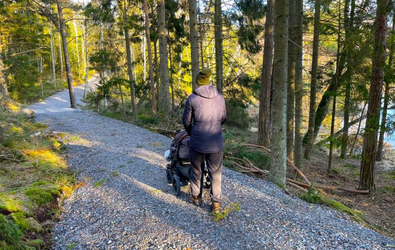 Person med barnvagn går på en grusväg omgiven av träd.