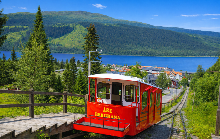 Röd linbana nedför en backe med utsikt över sjön och gröna omgivningar.