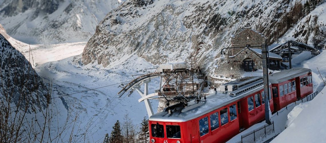 Röd linbana som åker uppför ett snöigt berg med dalgång nedan.