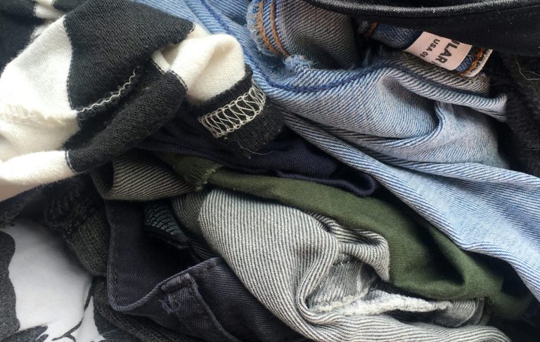 En hög med blandade kläder i olika färger och material.