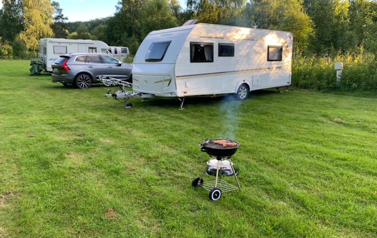 En campingvagn parkerad på grön gräsmatta med en kolgrill som rök utanför.