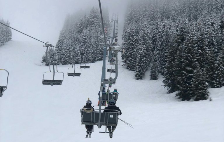 Skiåkare på en stollift med snöiga träd i bakgrunden.