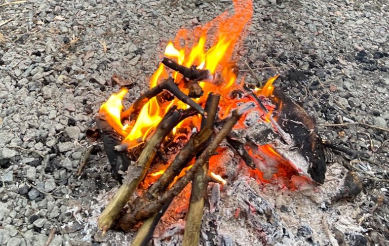 Eld som brinner på en stenig yta med ved och glödande flammor.