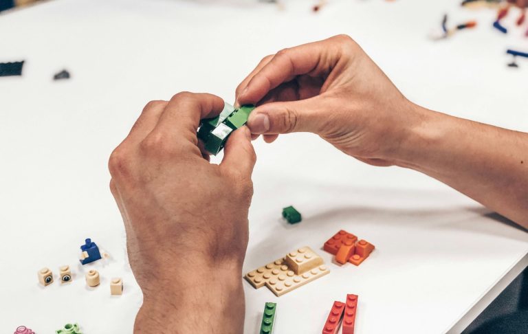 Händer som bygger med färgglada klossar på ett bord.