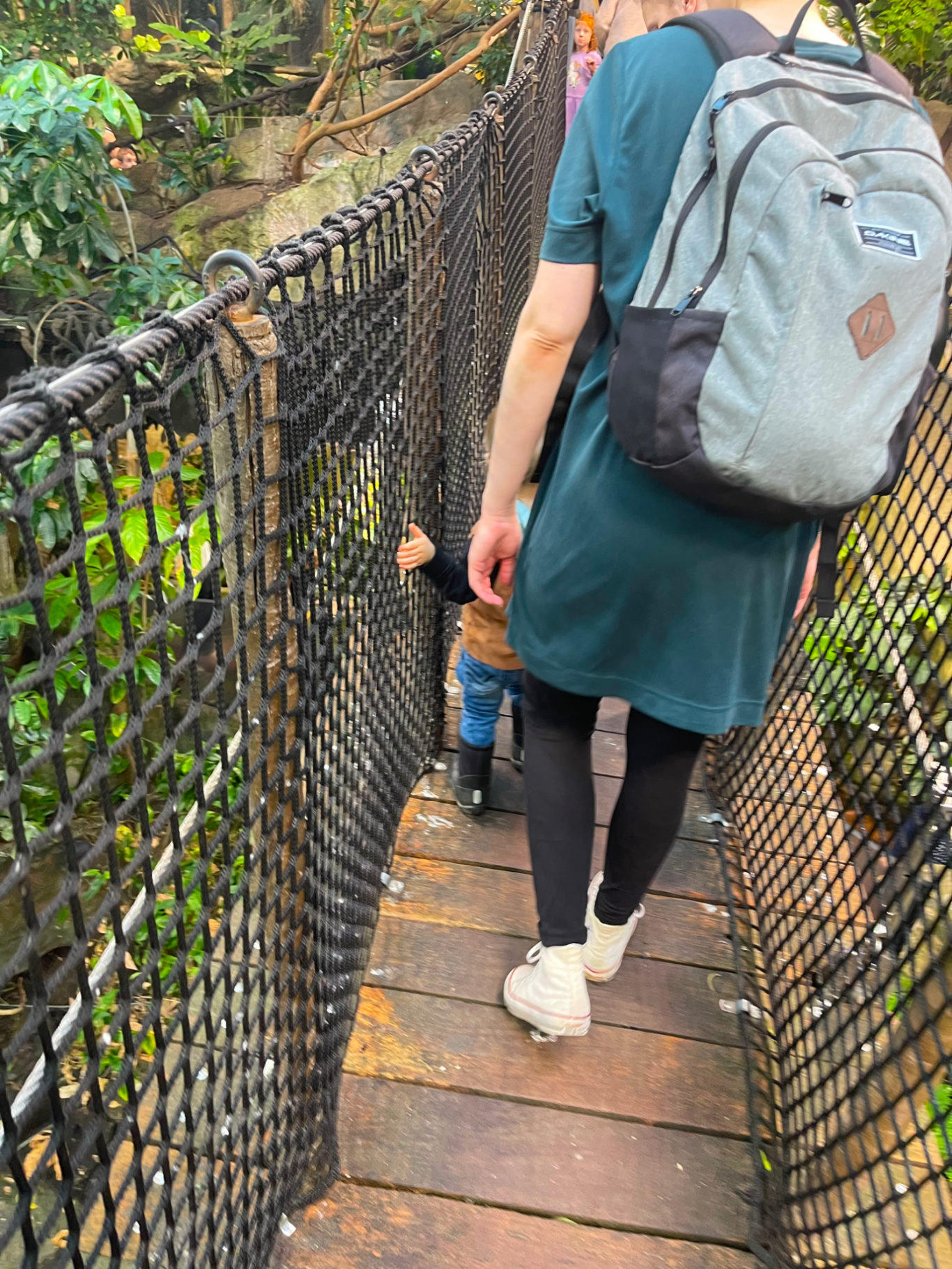 Djungeln Person i grön klänning går på en hängbro med ett barn. Grönska runt omkring.