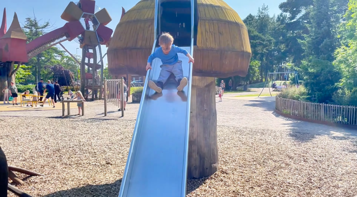 Vallarnas Friluftsområde Lekplatsen Ett barn åker ner för en rutschkana vid en lekplats med trädgårdsmiljö.