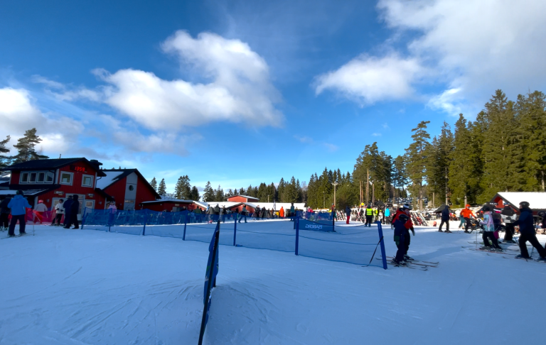 Skidåkare vid snötäckta backar, med ett blått avspärrningsband och träd i bakgrunden.