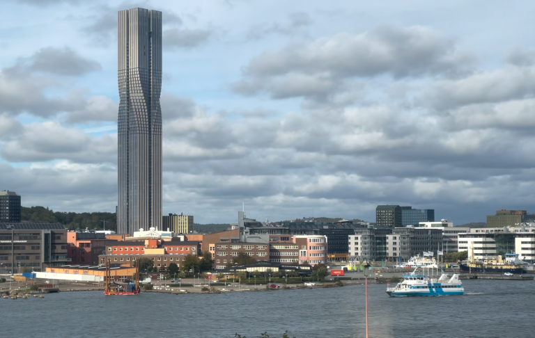 Skyskrapa i bakgrunden med hamn och fartyg i förgrunden under molnig himmel.