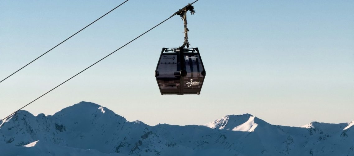 Gondol i Les 3 Vallees hänger i luften med snöiga berg i bakgrunden.