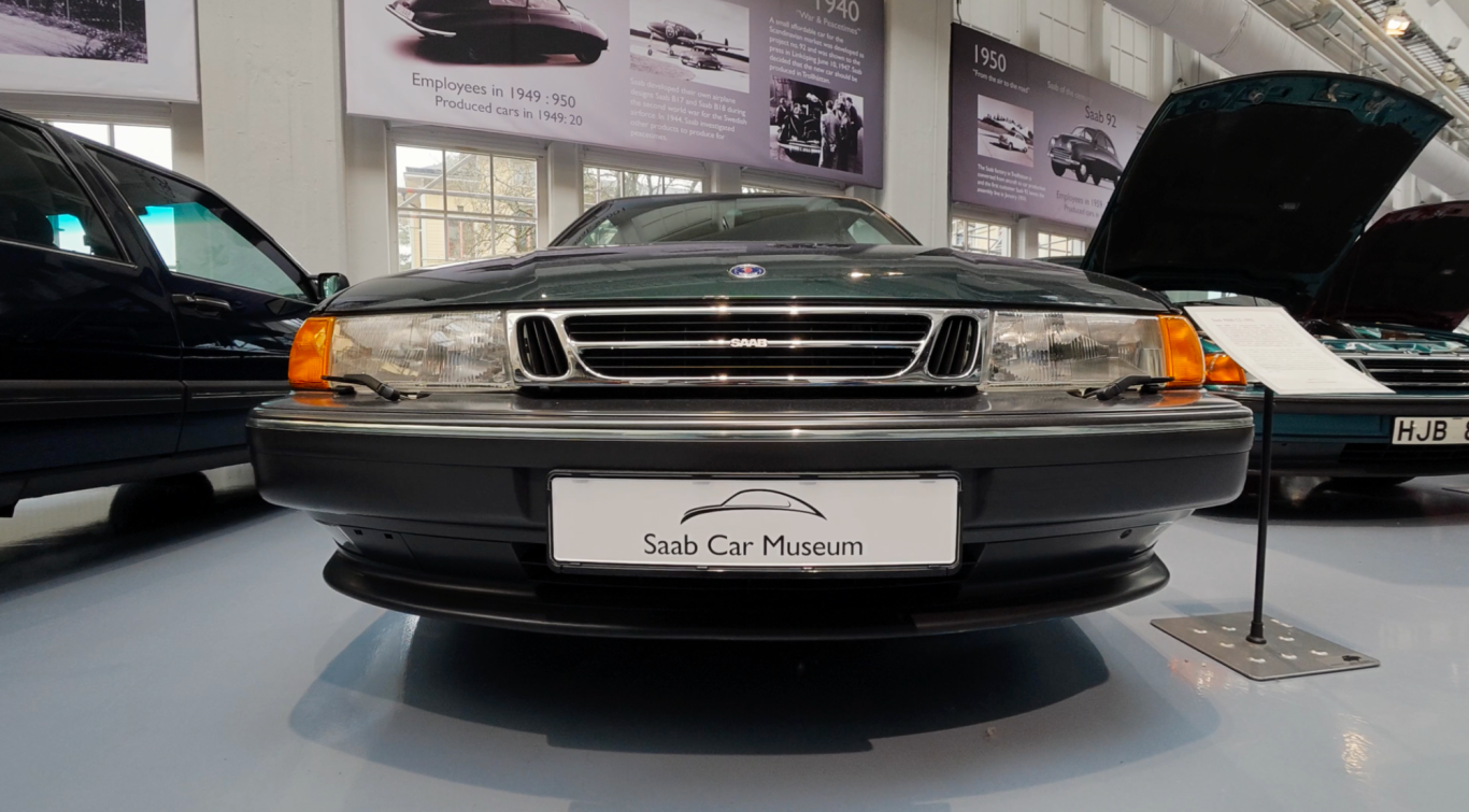 Saab 9000 Grön bil framifrån i ett bilar museum med utställda fordon i bakgrunden.