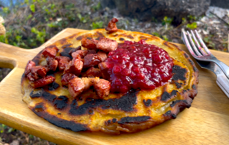 Bränd plätt med baconbitar och rårörd lingonsylt på en träskärbräda.