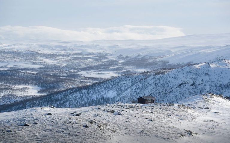 Snöklädda fjäll och vidsträckt dalgång under en klar himmel.