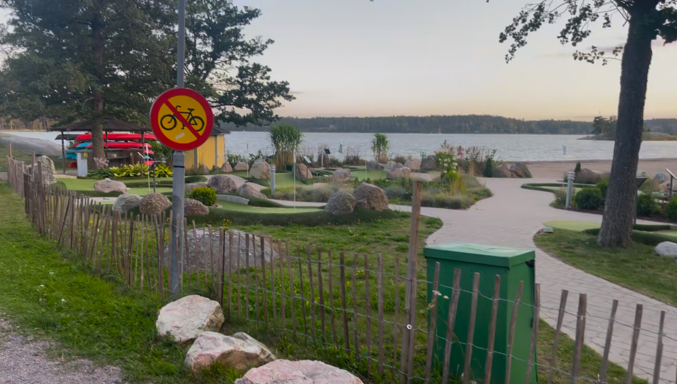 Minigolfbanan vid stranden Lugnt strandområde med blommor, stigar och en skylt om rökförbud.