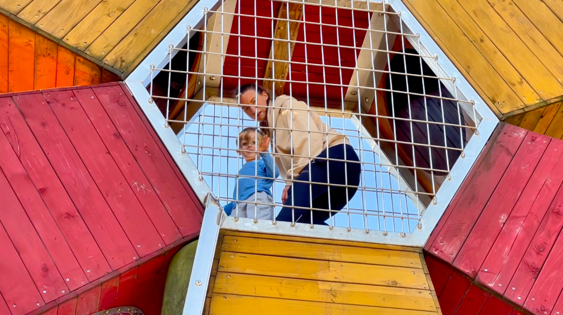 Vallarnas Friluftsområde LekplatsenVallarnas Friluftsområde Lekplatsen En vuxen och ett barn leker tillsammans i en färgglad lekställning.