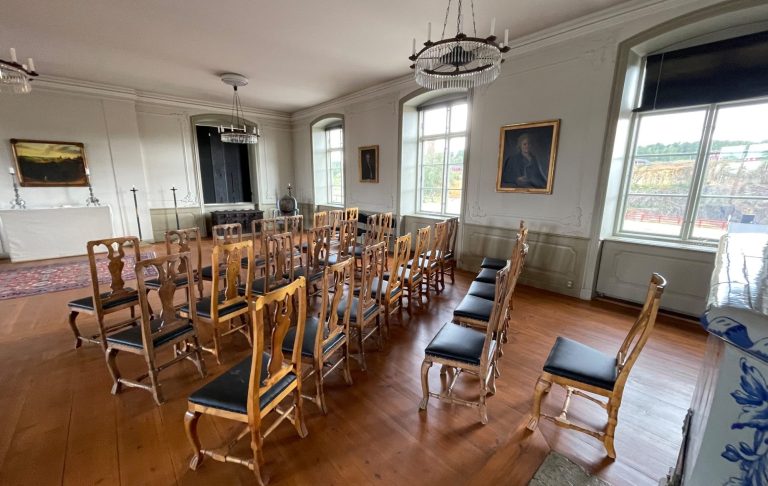 Ett rum med stolar i rad och ett stort fönster som släpper in ljus.