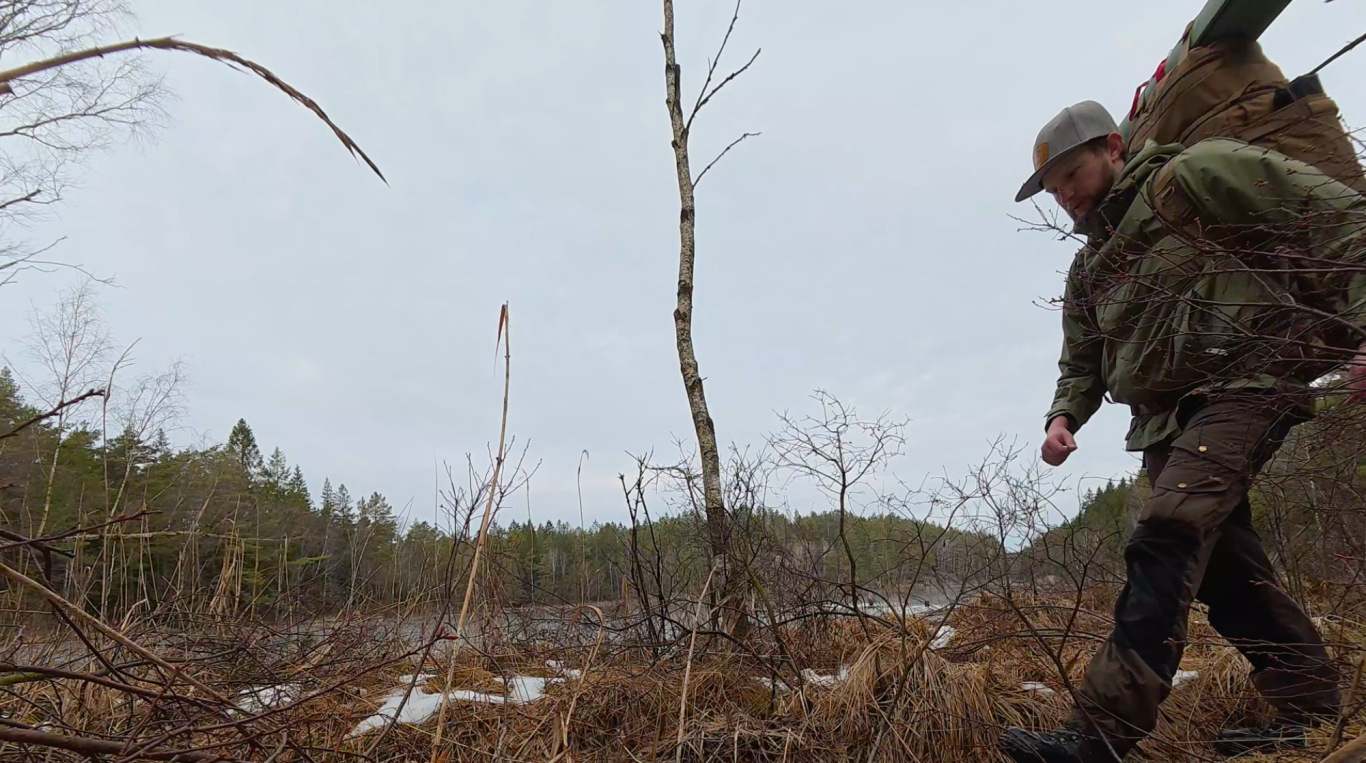 På väg hem Man går genom ett kargt landskap med en ryggsäck på ryggen. Sparse vegetation runt omkring.