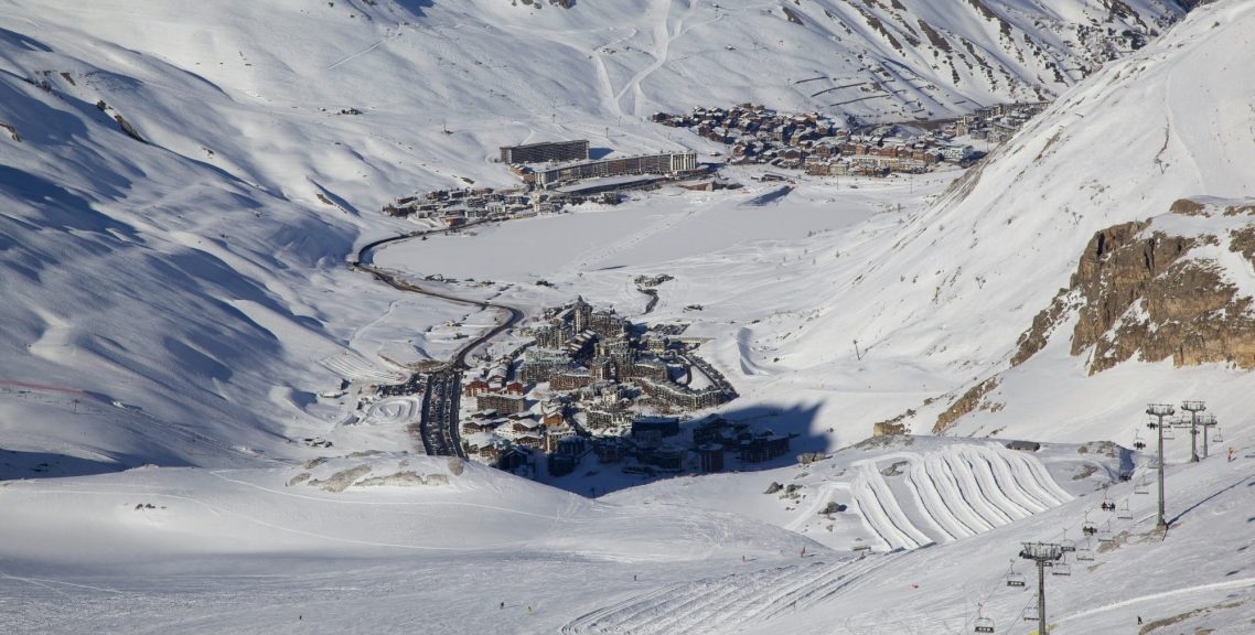 Utsikt över en snötäckt alpdal med fjäll, byggnader och liftar.