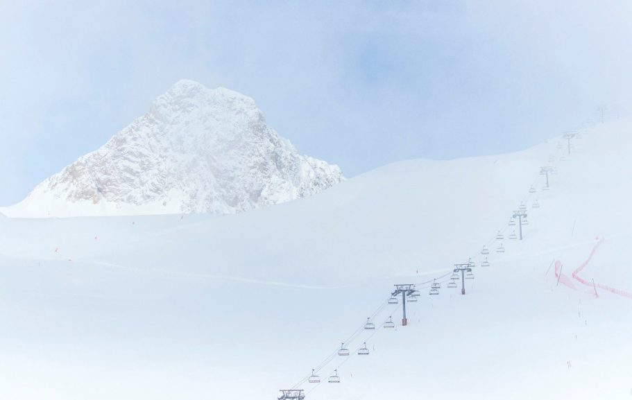 Snötäckta fjäll med liftar som leder upp mot en bergstopp.