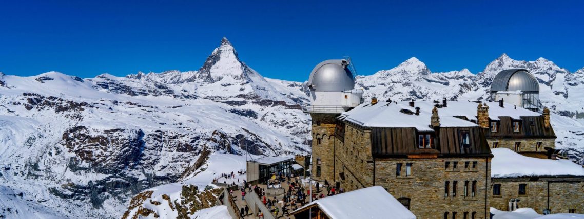 Snötäckta berg med Matterhorn i bakgrunden, byggnader med kupoler i förgrunden.