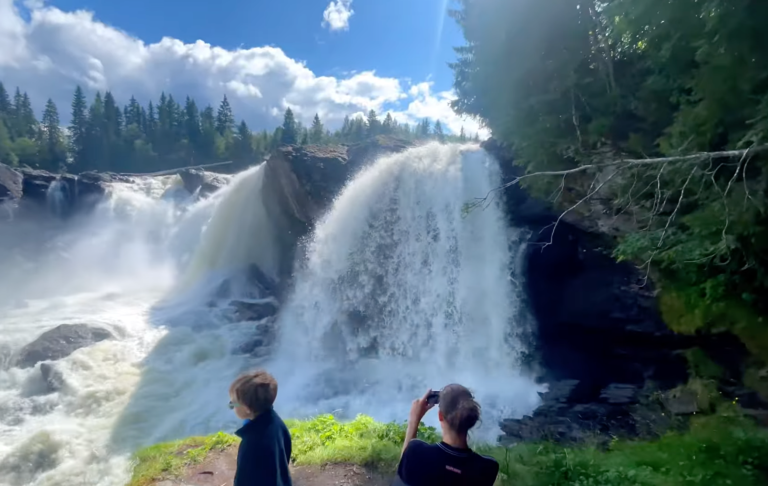 Vattenfall med kraftfull ström, omgiven av grönska och en klar himmel.