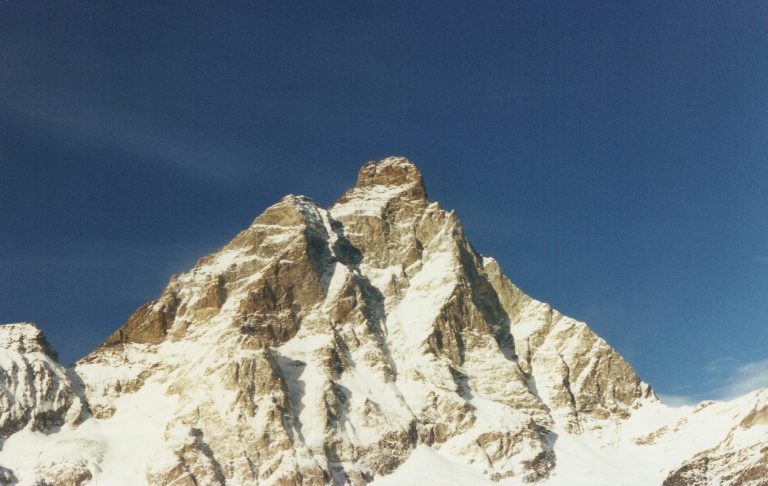 Snötäckta bergstoppar under en klarblå himmel.