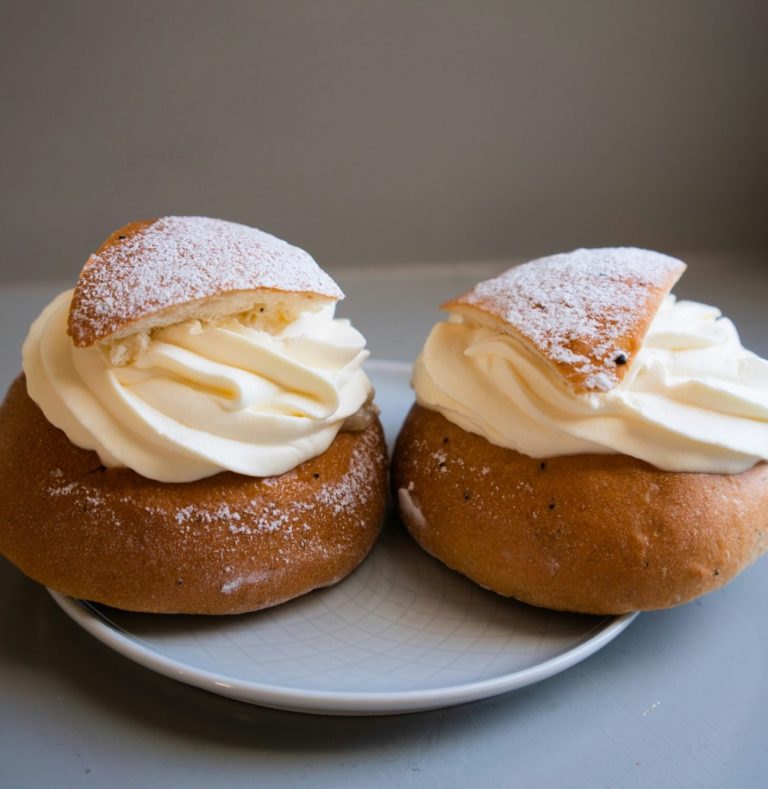 Två semlor med vispgrädde och ett lock av mandelmassa på ett fat.
