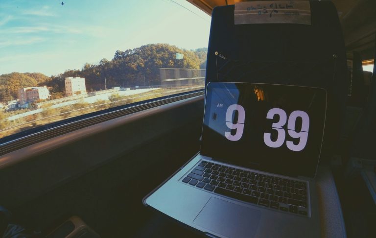 En bärbar dator med klocka som visar 09:39, utsikt genom ett tågfönster.