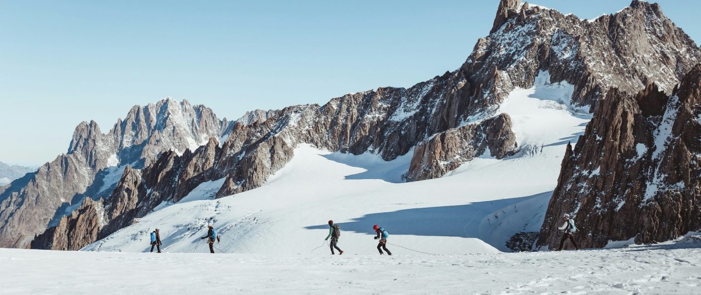 Courmayeur - Italien Skidåkare på en snötäckt bergsrygg med klippformationer i bakgrunden.